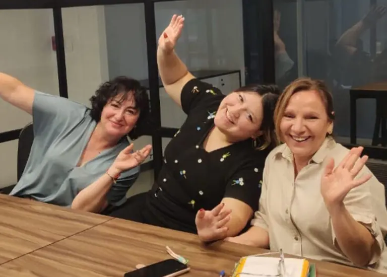 Un grupo de estudiantes sonriendo y colaborando juntos alrededor de una mesa de estudio en una sala de clases moderna de Alfabeta Chile.