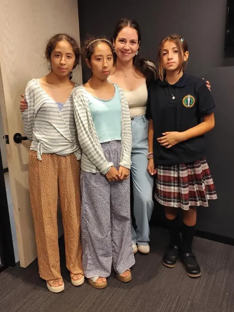 Un grupo de alumnas sonrientes posando junto a su profesora en un salón de clases moderno y luminoso de Alfabeta.