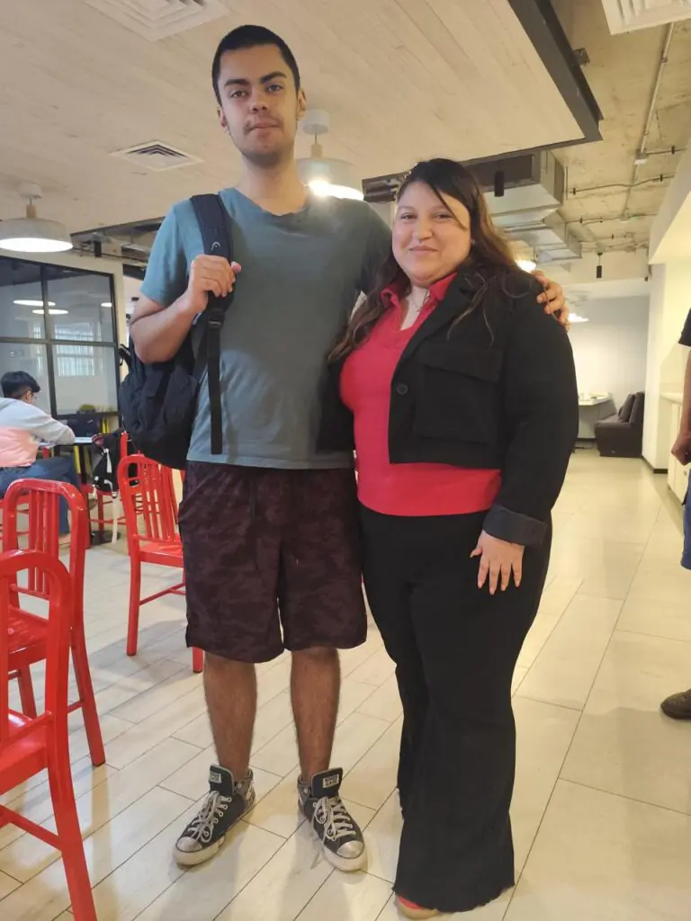 Una estudiante joven y su profesora de Alfabeta posando juntas con expresiones de confianza y satisfacción.