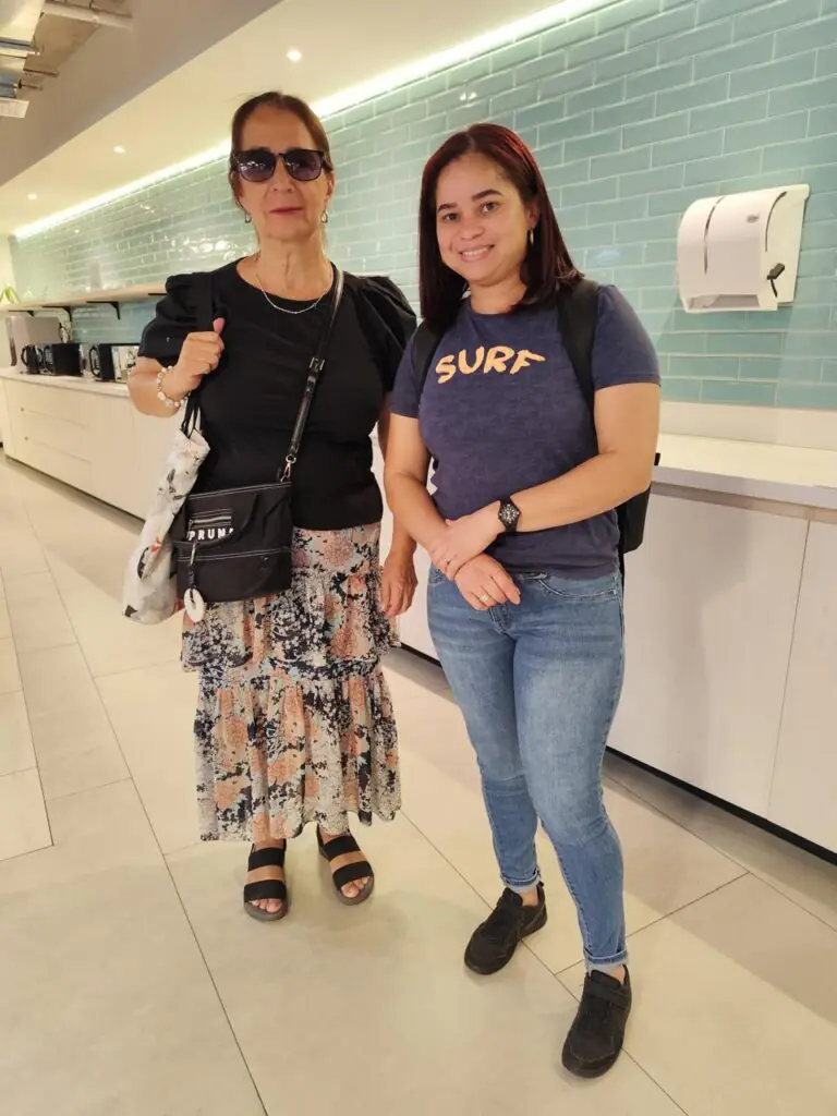 Una mujer adulta posando felizmente con una profesora, demostrando satisfacción por sus avances en comprensión lectora.