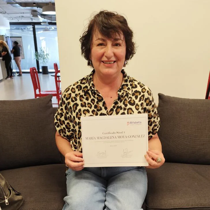Primer plano de una mujer mostrando su certificado de Alfabeta, donde se aprecia el logo y el nombre del programa.