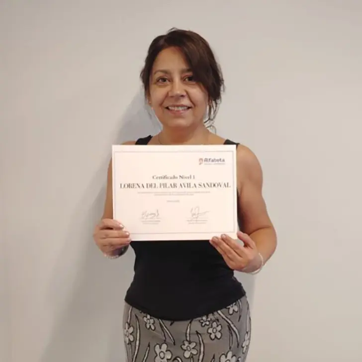 Mujer posando con su diploma frente a las instalaciones del centro Alfabeta, como si compartiera su experiencia.