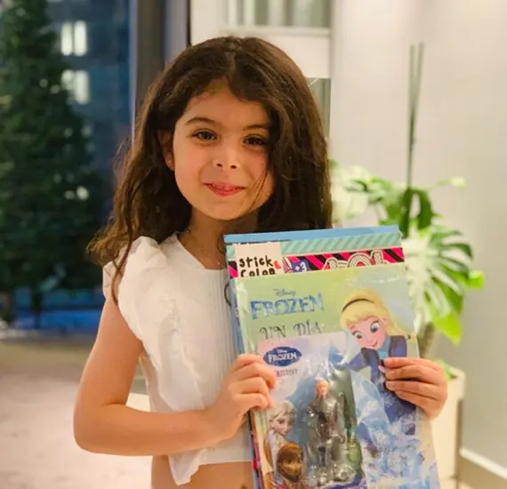 Niña sosteniendo con alegría varias revistas infantiles, sugiriendo el placer de tener acceso a diversidad de historias y conocimientos.