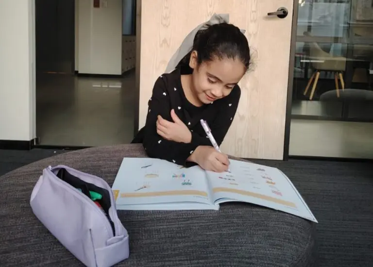 Niña pequeña sentada cómodamente en su escritorio, rodeada de libros coloridos y materiales didácticos.