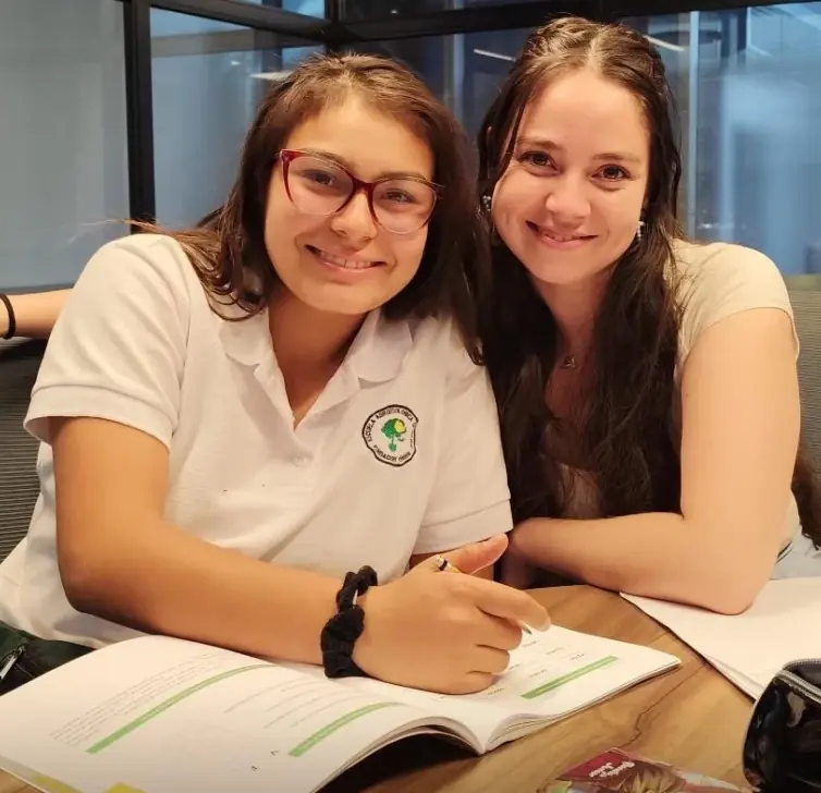 Profesora guiando a un alumno niño en la lectura de un libro de ejercicios.